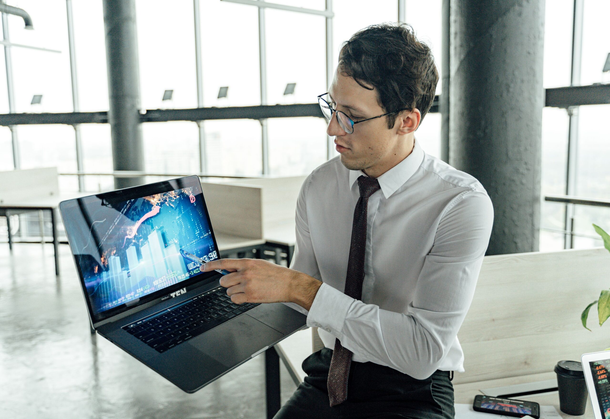 A businessman in an office analyzing market trends on a laptop with graphs and charts displayed.